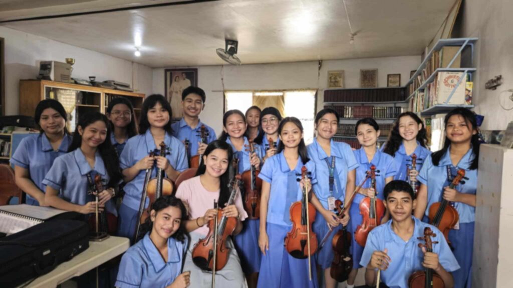 students at our our private Christian school in Mandaue during their music class holding violin and other musical instrument, smiling ear to ear with their music teacher